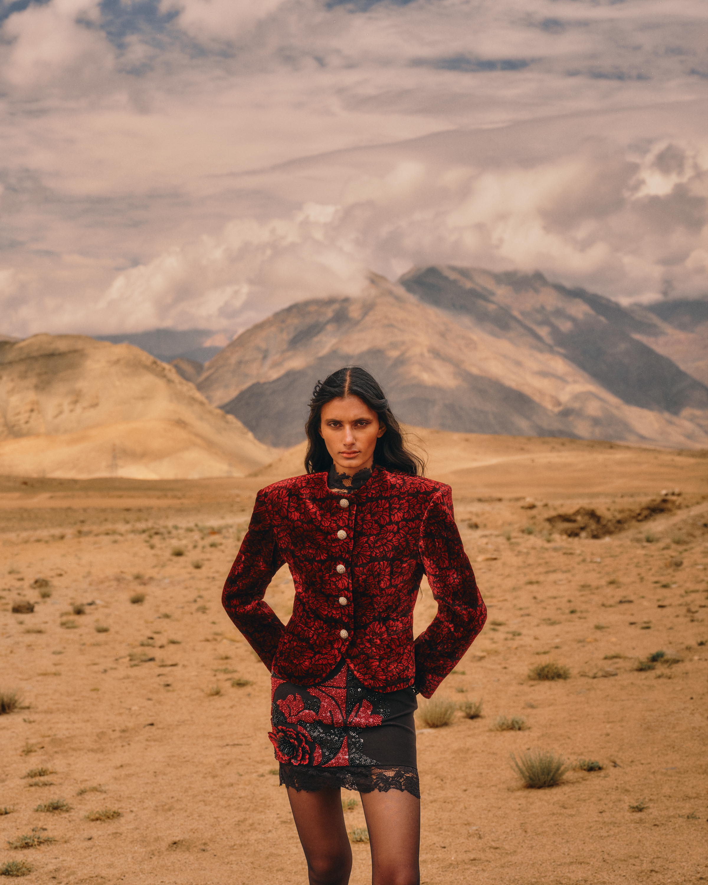 Model in a red and black patterned jacket and embellished skirt against Ladakh’s mountains