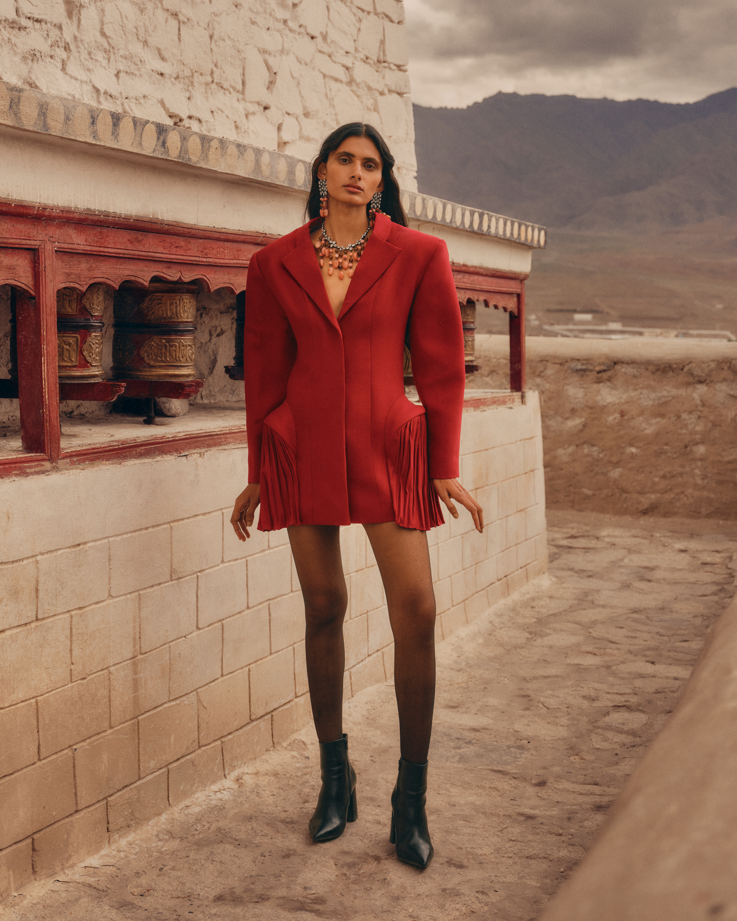 Model in a red tailored dress beside prayer wheels in Ladakh