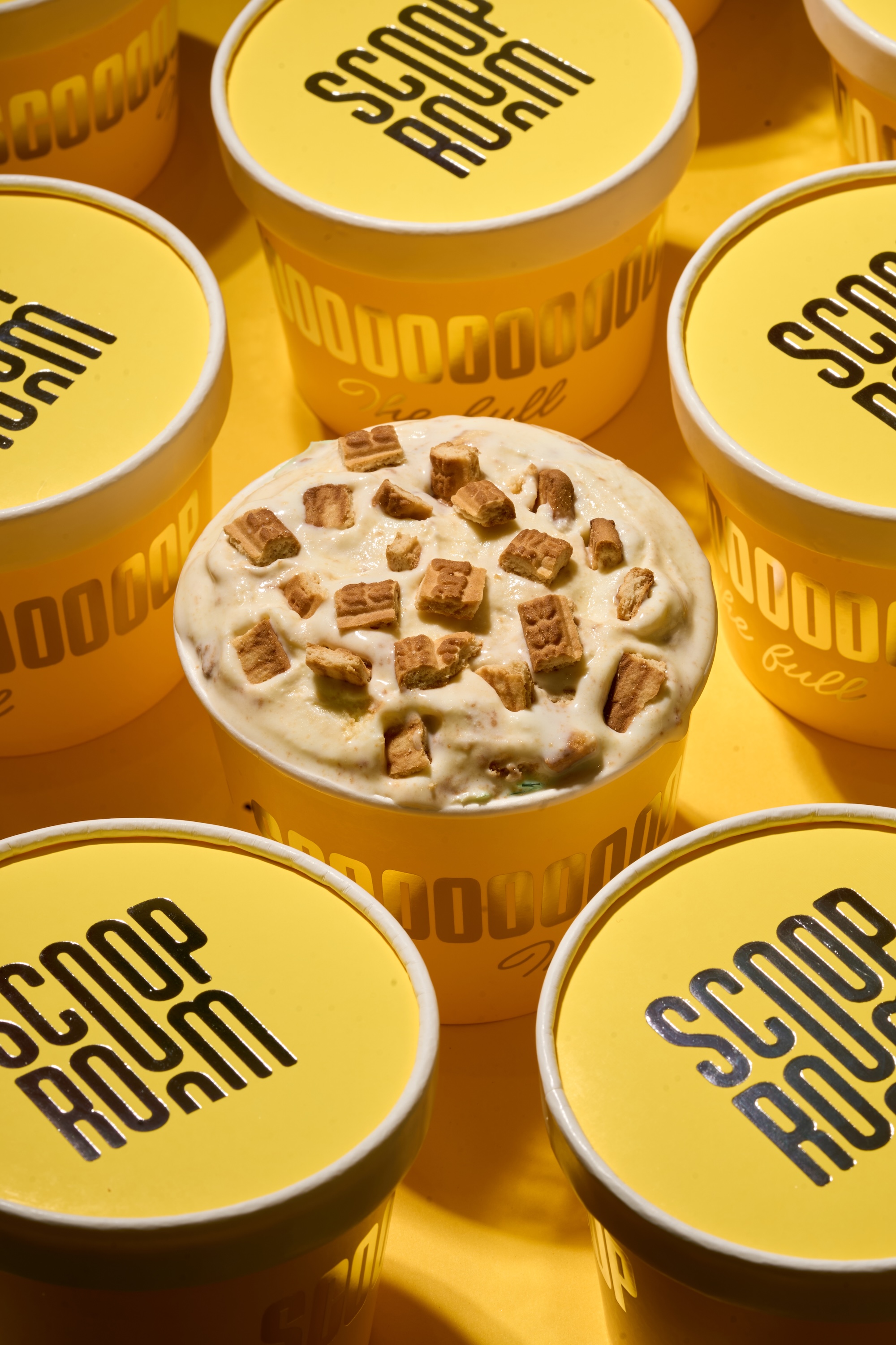 Ice cream topped with biscuit pieces in a yellow Scoop Room tub