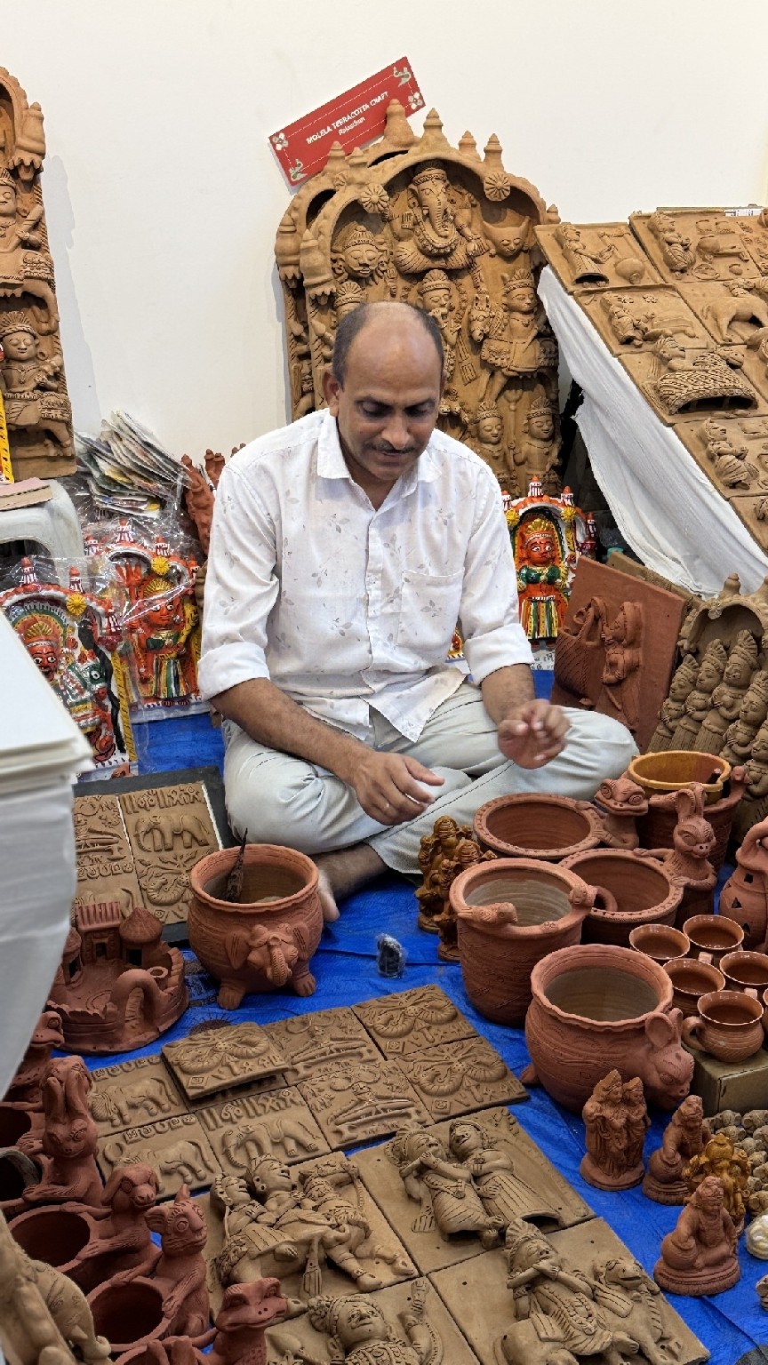 A terracotta artisan surrounded by handmade pots and relief panels